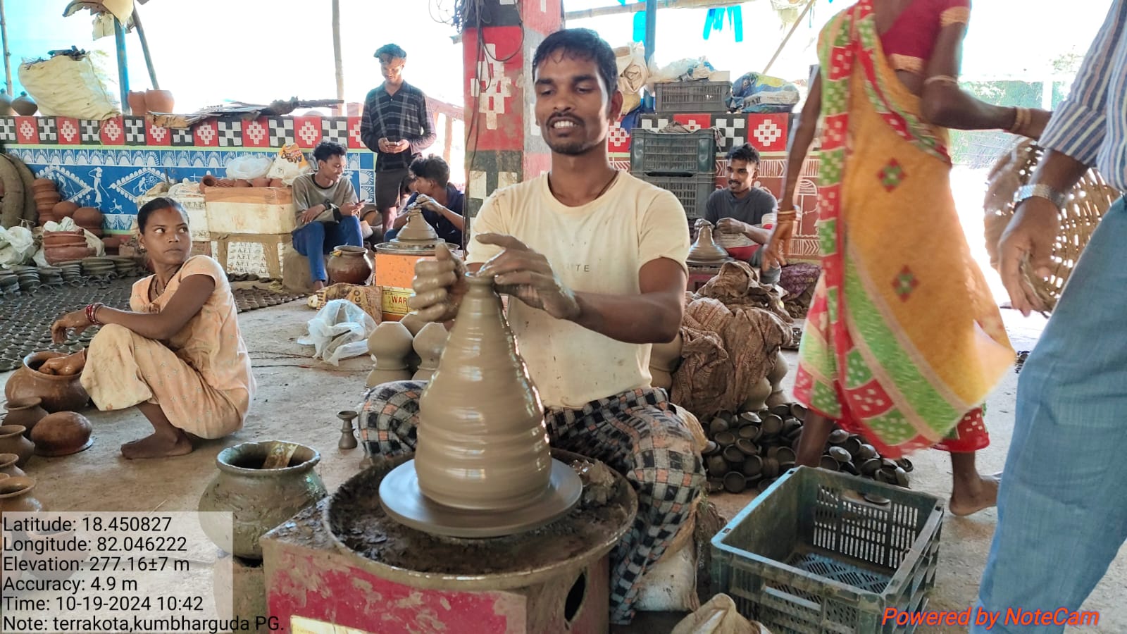A potter shaping a tall clay vessel on a wheel inside the Kumbharguda workshop