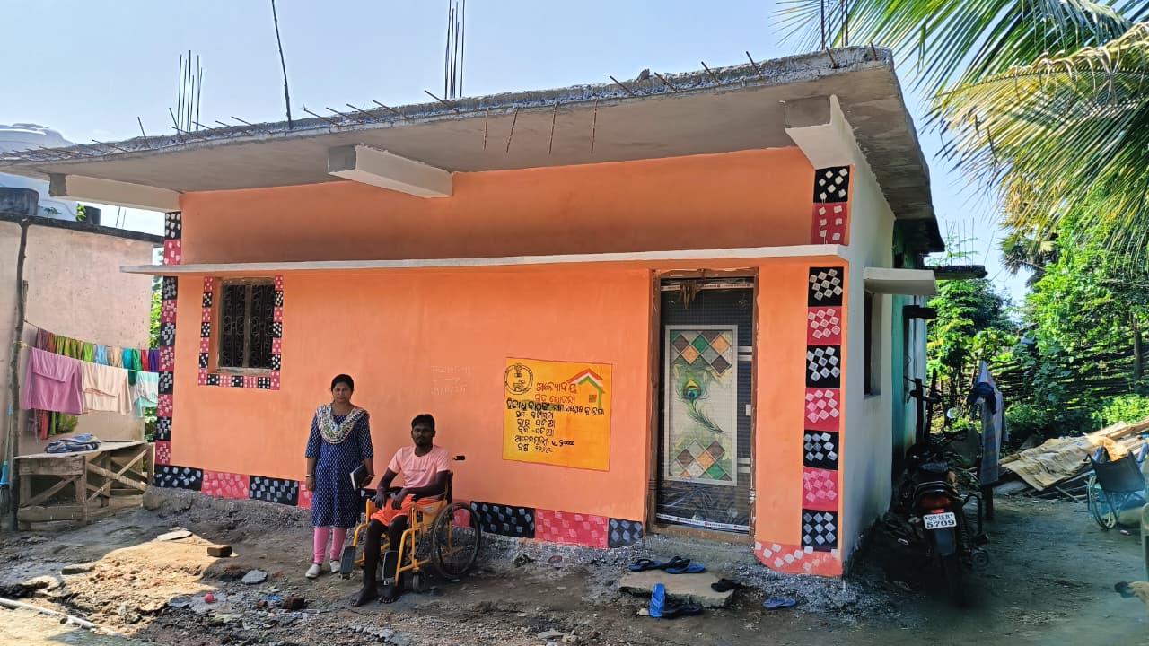 Santosh Kumar Nupa and a family member in front of their completed orange house in Podia