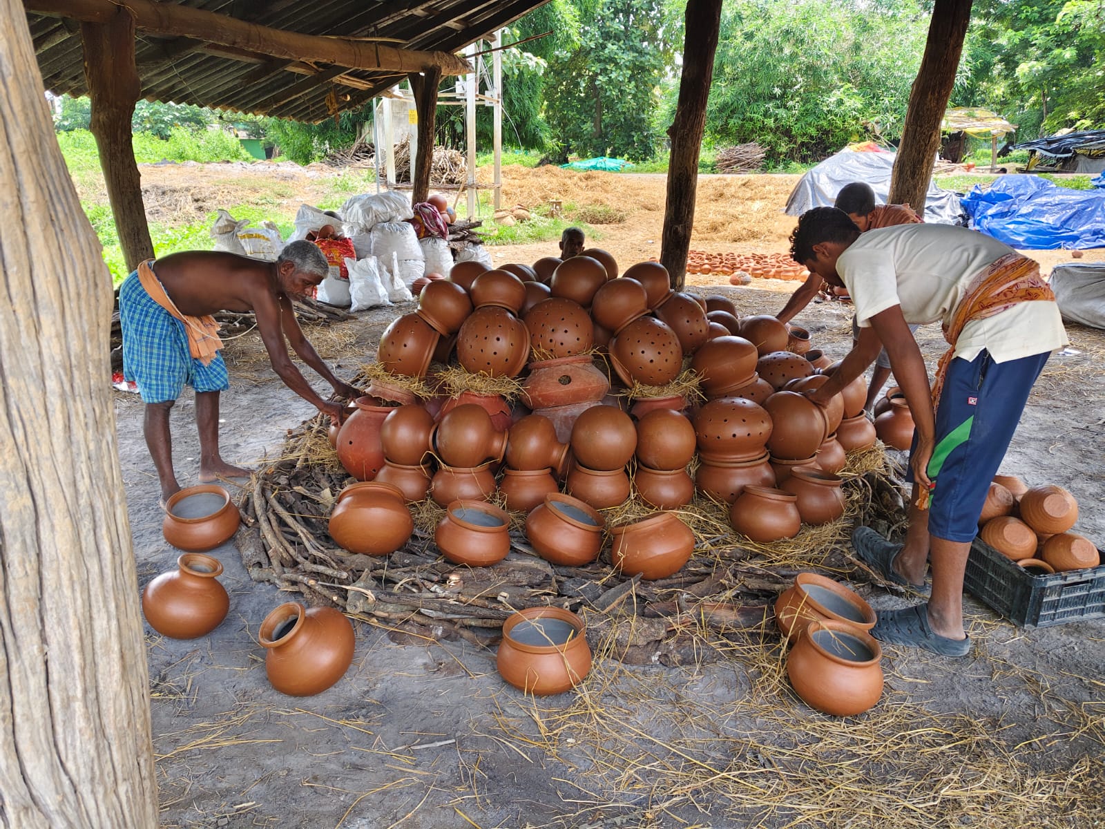 Potters arranging a large group of finished clay pots under a workshop shelter