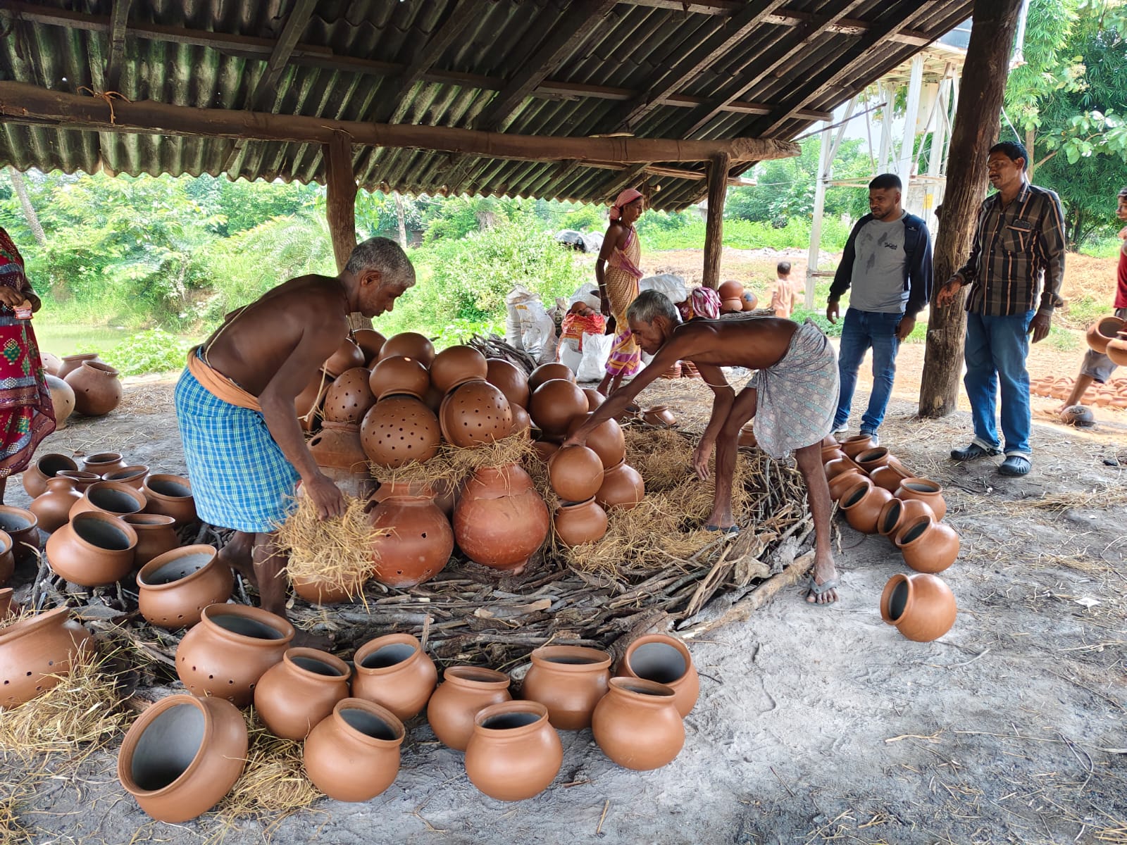 Potters stacking clay vessels with straw and wood for firing